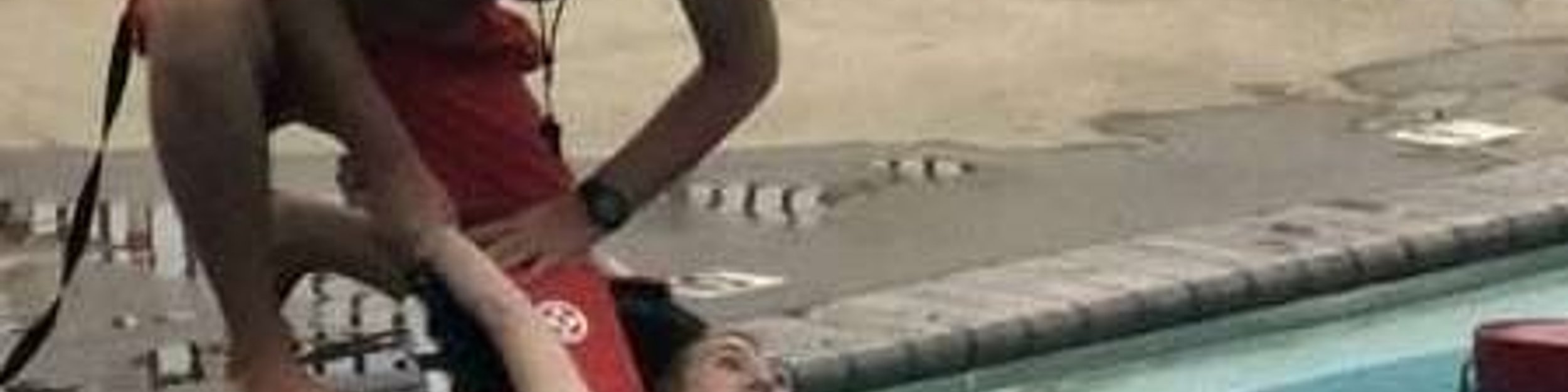 Lifeguard candidates practicing a backboard rescue at an outdoor pool